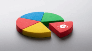 Colorful circular pie chart made of foam segments in red, green, blue, and yellow, with the red piece separated and showing a white light bulb icon