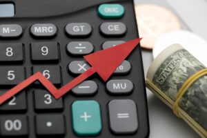 close up of a calculator with upward arrow and folded dollar bills beside the calculator