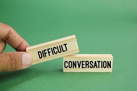Hand placing a block labeled “Difficult” next to another labeled “Conversation” on a green background.