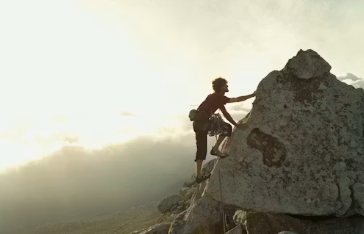 Person climbing a rocky mountain peak against a sunset