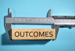 Caliper measuring a wooden block labeled “OUTCOMES.”
